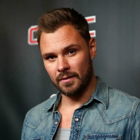 Patrick Flueger in a blue jacket looks at the camera.